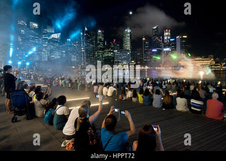 I turisti scattano fotografie e film di 'Wonder Full' - un acqua, luce, musica e spettacolo di laser a Singapore di notte. Foto Stock