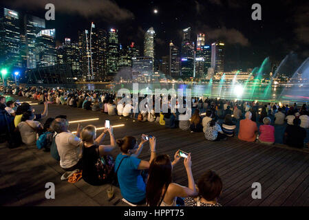 I turisti scattano fotografie e film di 'Wonder Full' - un acqua, luce, musica e spettacolo di laser a Singapore di notte. Foto Stock