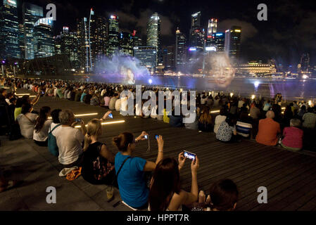 I turisti scattano fotografie e film di 'Wonder Full' - un acqua, luce, musica e spettacolo di laser a Singapore di notte. Foto Stock