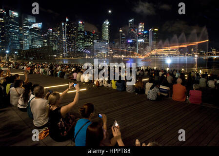 I turisti scattano fotografie e film di 'Wonder Full' - un acqua, luce, musica e spettacolo di laser a Singapore di notte. Foto Stock