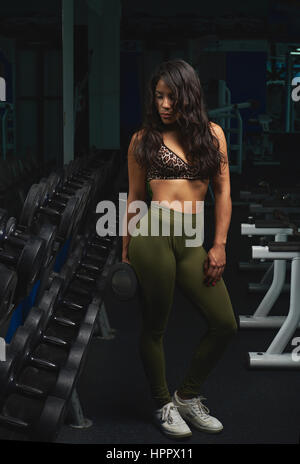 Skinny donna che lavorano con manubri in palestra moderna. Bruna giovane donna tenendo i pesi facendo allenamento Foto Stock