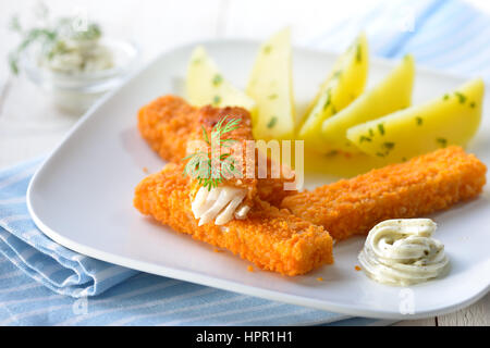 Croccante di bastoncini di pesce impanati di pollack filetto servito con patate con prezzemolo e salsa remoulade su una piastra bianca - il fuoco selettivo Foto Stock