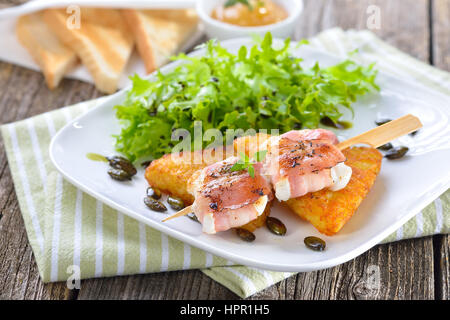 Arrosto di formaggio di capra avvolto in pancetta affumicata e servita su croccante di hash browns fritto con semi di zucca, insalata e la fig la senape Foto Stock