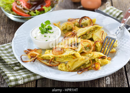 Fritti ravioli sveva (cosiddetto'Maultaschen') con riempimento vegetariano servito con cipolle arrosto, uova strapazzate e crema di formaggio alle erbe Foto Stock