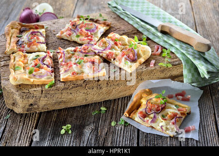 Al forno caldo tarte flambee dall'Alsazia con cipolla e pancetta e panna acida servita su una squallida tagliere di legno Foto Stock