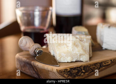 Parmigiano e altri vari formaggi sul tagliere di legno. Sullo sfondo di una bottiglia di vino italiano con vetro originale. Profondità di campo. Foto Stock