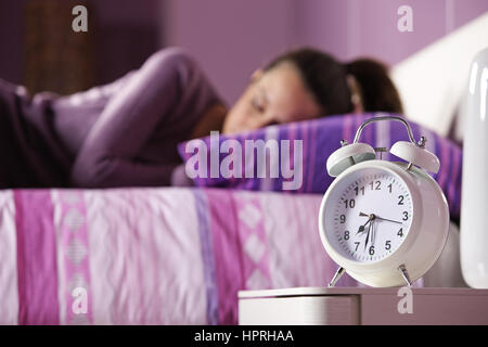 Un orologio sveglia con un sonno giovane donna in background Foto Stock