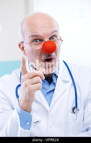 Funny senior medico con red clown naso e espressione divertente. Foto Stock