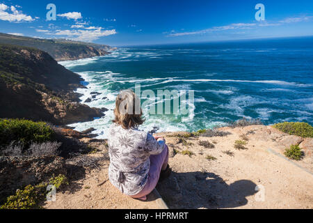 Escursionista donna seduta fotografica posteriore affacciato sulla scogliera rocciosa costa con blu oceano verso l'orizzonte. Foto Stock