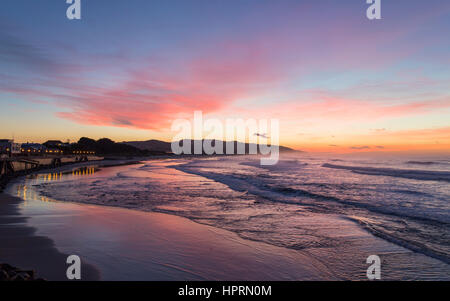 Dunedin, Otago, Nuova Zelanda. Vista sull'Oceano Pacifico su St Clair Beach all'alba, rosa sky riflessa nell'acqua. Foto Stock