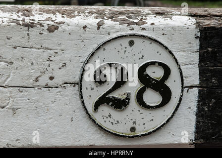 Il numero 28 nero su bianco in un bordo circolare verniciato contro un bianco e nero lo sfondo di legno. Foto Stock