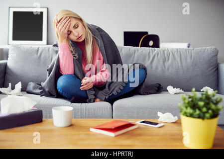 Malata con mal di testa seduto sotto la coperta Foto Stock