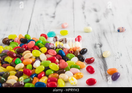 Candy Jelly Beans di diversi colori sul luminoso in legno dipinto di bianco sullo sfondo. Spazio per il testo Foto Stock