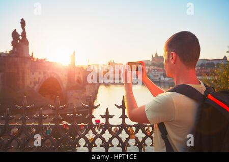 Viaggiatore con zaino prendendo foto dal telefono cellulare. Giovane turista vicino al Ponte Carlo al tramonto. Praga, Repubblica Ceca. - Back lit Foto Stock