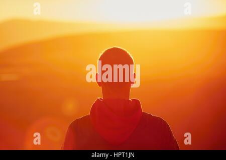 Un tramonto meraviglioso. Silhouette del giovane uomo sulla cima della montagna. - La retroilluminazione con riflessioni di Sun Foto Stock