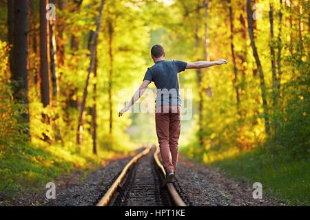 Orario estivo - Giovane godendo il viaggio. A piedi sul tracciato ferroviario nel bosco al tramonto. Foto Stock