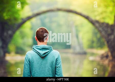 Pensieroso giovane uomo su il pond bank. - Un posto stupendo in Germania. Rakotzbrucke noto anche come ponte di diavoli in Kromlau. Foto Stock