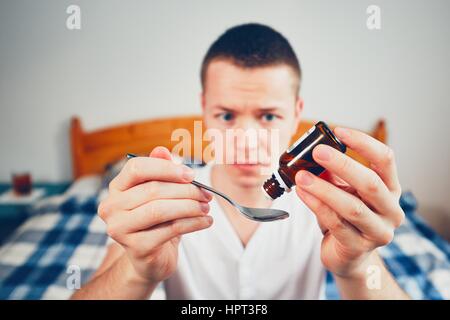 Uomo malato in camera da letto. Messa a fuoco selettiva su gocce farmaco sul cucchiaio. Foto Stock