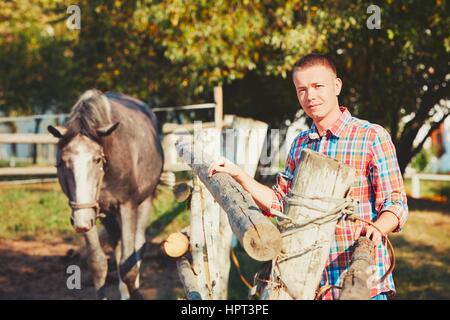 Giovane uomo e cavallo nella fattoria di campagna nel giorno d'estate. Foto Stock
