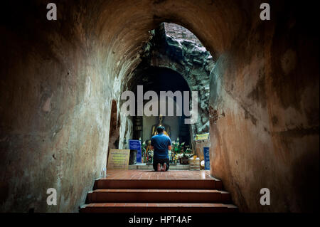 WAT UMONG, Chiang Mai, Thailandia - Giugno 2015 - un uomo si inginocchia in preghiera prima di un dorato statua del Buddha in un sotterraneo altare al Wat Umong, Chiang Mai Foto Stock