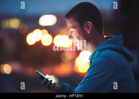 Solo nella notte in città con il telefono cellulare. Bello dreamy uomo messaggio di lettura (o cercando sul video) sul suo smartphone. Foto Stock