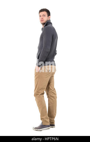 Vista laterale del casual uomo in maglione a piedi guardando la telecamera su spalla. Corpo pieno lunghezza ritratto isolate su sfondo bianco. Foto Stock