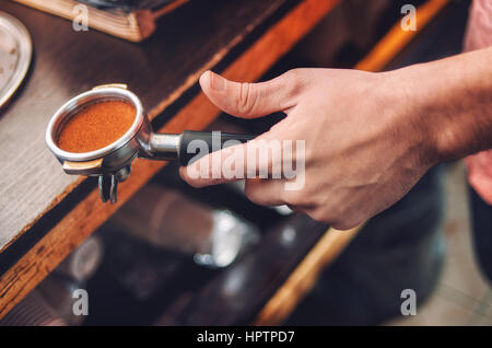 Primo piano della mano con i baristi titolare con caffè appena macinato. Soft focus Foto Stock