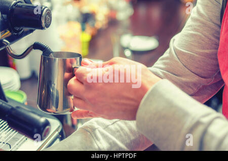 Stretta di mano barista fruste il latte per il caffè espresso presso la macchina del caffè in un accogliente bar. Soft focus. Foto Stock