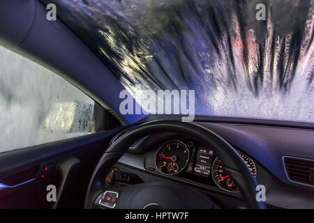 Auto in una stazione di lavaggio automatico sito, schiuma detergente viene spruzzato sulla, ruotare la spazzola di pulizia Foto Stock
