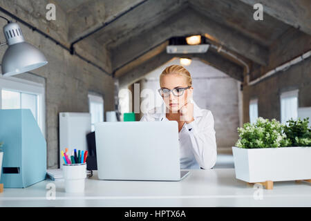 Considerato occupato business donna lavora su computer portatile presso un ufficio moderno Foto Stock