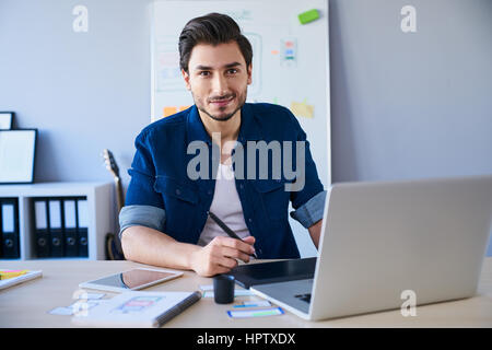 Ritratto di designer grafica freelance seduto alla scrivania con computer portatile e tablet Foto Stock