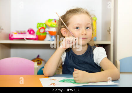 Adorabile ragazza bambino disegna una spazzola e vernici in nursery room. Bambino in asilo nido in Montessori classe di età prescolare. Foto Stock