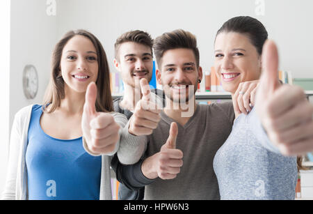 Allegro gruppo di studenti sorridente in telecamera con il pollice in alto, il successo e il concetto di apprendimento Foto Stock