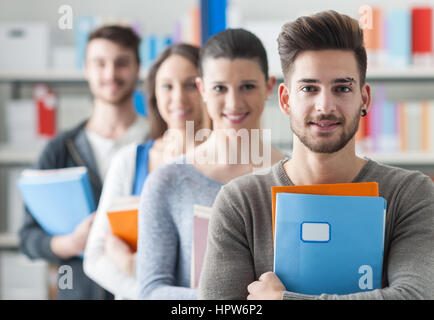 Un gruppo di studenti del college nella libreria in piedi in linea e guardando la telecamera, la conoscenza e lo studio concept Foto Stock