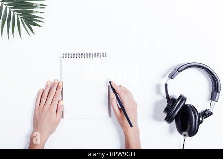 Mani femminili, notebook e cuffie su un tavolo bianco vista superiore Foto Stock