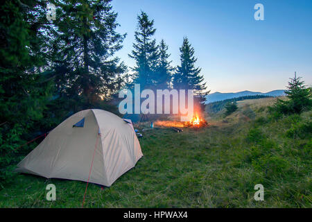 Tenda per gli escursionisti in montagna in serata con un falò con scintille vicino Foto Stock