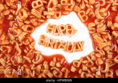 Buon compleanno scritto in spaghetti lettere circondato con lettere illeggibili. Foto Stock