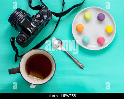 Colorate macaron francese,tazza di tè e fotocamera reflex su sfondo verde-vista superiore Foto Stock