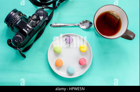 Colorate macaron francese,tazza di tè e fotocamera reflex su sfondo verde-vista superiore Foto Stock