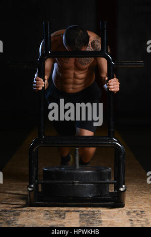 Uomo muscolare facendo Peso pesante esercizio velocità ponderata Sled In Palestra Foto Stock