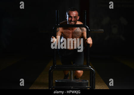 Uomo muscolare facendo Peso pesante esercizio velocità ponderata Sled In Palestra Foto Stock