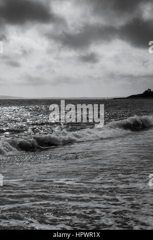 Foto in bianco e nero di un cielo tempestoso sulle onde che si infrangono sulla spiaggia di ciottoli a Ringstead Bay, Dorset, Regno Unito Foto Stock