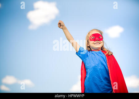 Funny bambina potenza di riproduzione super eroe oltre il cielo blu sullo sfondo. Concetto di supereroi. Foto Stock