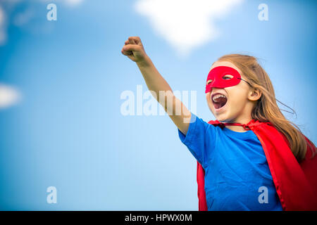 Funny bambina potenza di riproduzione super eroe oltre il cielo blu sullo sfondo. Concetto di supereroi. Foto Stock