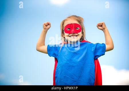 Funny bambina potenza di riproduzione super eroe oltre il cielo blu sullo sfondo. Concetto di supereroi. Foto Stock