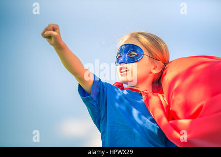 Funny bambina potenza di riproduzione super eroe oltre il cielo blu sullo sfondo. Concetto di supereroi. Foto Stock