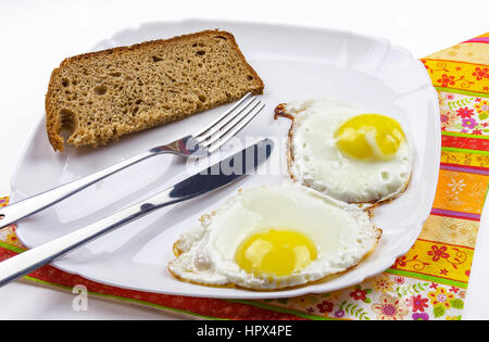 Sulla piastra bianca è due uova fritte e una fetta di pane nero Foto Stock
