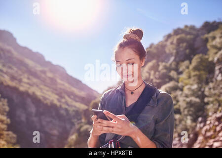 Giovane donna texting con un telefono cellulare al di sotto di rupi assolate Foto Stock