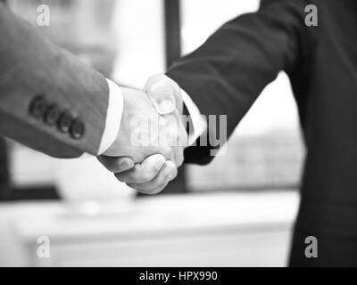 Due uomini di affari aziendali stringono le mani in ufficio, in bianco e nero. Foto Stock