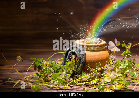 Il giorno di San Patrizio decorazione con luce magica rainbow pentola piena di monete d'oro, a ferro di cavallo e trifogli su vintage sfondo di legno, close up Foto Stock